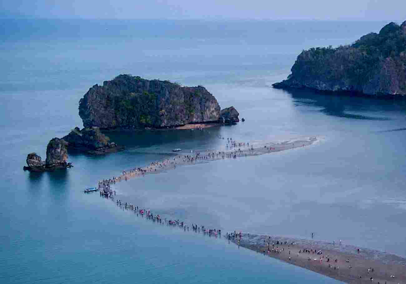 Image of people walking across a vast sandbar connecting an island and the beach.